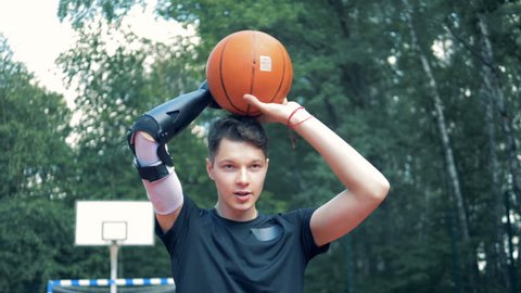 Teenage boy with a prosthetic hand is throwing a basket-ball.