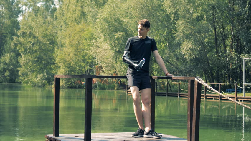River bridge with a young man standing on it and drinking with his artificial hand
