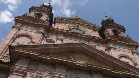 Mannheim, Baden-Württemberg, Germany. July 17. 2018, High angle shot of twin towered facade of red sandstone of Mannheim Jesuit Church. CAmera tilts down along the facade to the entryway with elaborat