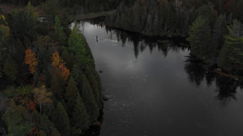 Aerial Perspective of Autumn Forest During Cloudy Day & A Man Paddle-Boarding on The Lake