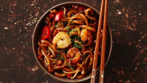 Traditional asian udon stir-fry noodles with shrimp in bowl and chopsticks. Fresh chilli pepers on side. Placed on dark rusty background with copy space.