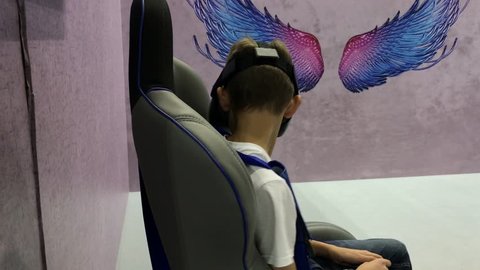 Brno, Czech Republic - 10/20/2018: Teenager in augmented reality glasses siting on virtual reality chair and looking to virtual show. Young person in virtual reality headset play with game simulator
