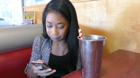 A cute 12 year old Asian girl enjoys spending time with her friend and sipping a yummy milkshake.