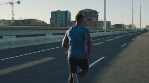 muscular african american man running in city road jogging athletic male exercising endurance workout in urban street at sunrise close up