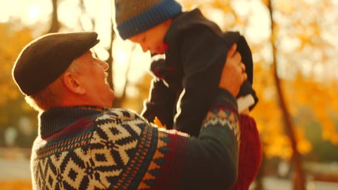Grandfather tossing his grandson in the arms in autumn park