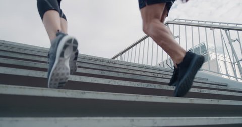two athletic runners legs running up stairs friends training together in urban city doing intense cardio exercise close up