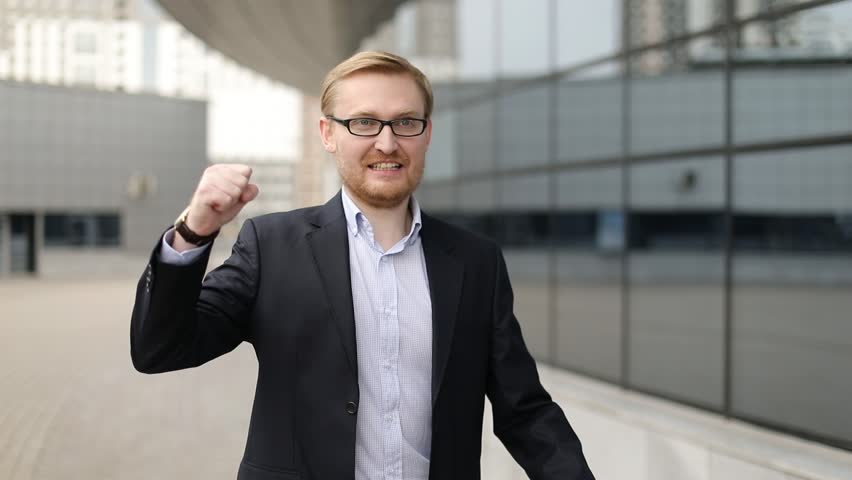 Businessman with arms raised celebrating success on the street. Steadicam shot, slow motion