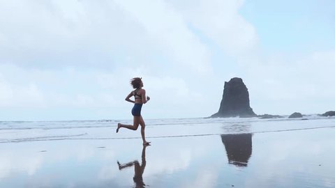 Barefoot sporty girl with slim body running along sea surf by water pool to keep fit and health. Beach background with blue sky. Woman fitness, jogging sports activity on summer family vacation.: film stockowy