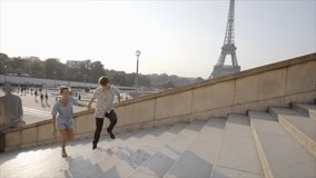 Young couple in Paris running up the stairs in front of the Eiffel Tower, France. Loving young people enjoying vacations and traveling in capital cities. 