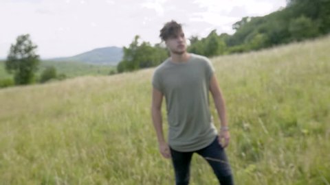 A young man is walking over a field in slow motion. His facial expression looks very thoughtful.