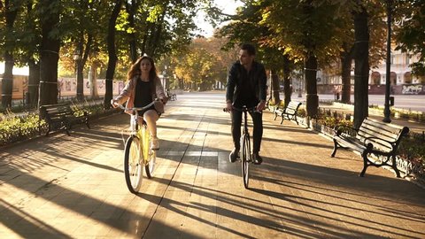 Front view of a young couple or friends riding their bikes in the city park or boulevard in summertime. People, leisure and lifestyle concept