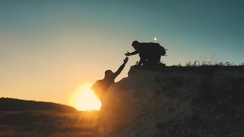 Silhouette of helping hand between two climber. two hikers on top of the mountain, a man helps a man to climb a sheer stone. couple hiking help each other silhouette in mountains with sunlight.