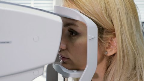 Woman looking at refractometer eye test machine in ophthalmology.