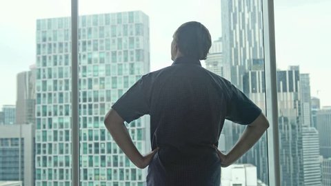 Young successful rich man comes to the window and admire the city center with skyscrapers view. 3840x2160