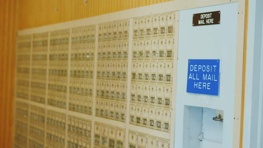 A young woman in glasses throws a few letters in the mailbox at the post office