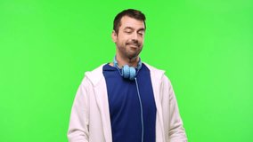 man with sweatshirt and music headphones on green screen chroma key background presenting and inviting to come with hand