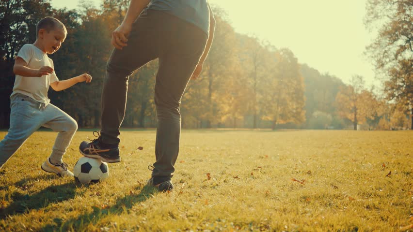 Father and son Soccer players in dynamic action funny play on the sand in  football in grass, summer sunny day under sunlight. | Shutterstock HD Video #1018245280