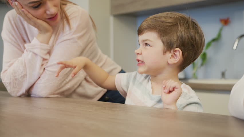 Boy sitting at a table and making funny faces.