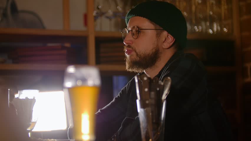Bearded man in glasses drinking beer in the bar | Shutterstock HD Video #1018257988
