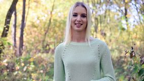 A video of a beautiful blonde girl in a park in the forest shows different emotions. She is standing right in front of the camera, smiling and looking happy.