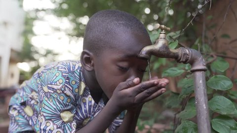 Handsome African boy drinking clean, fresh water from a tap just outside Bamako, Mali in a rural tribal village.