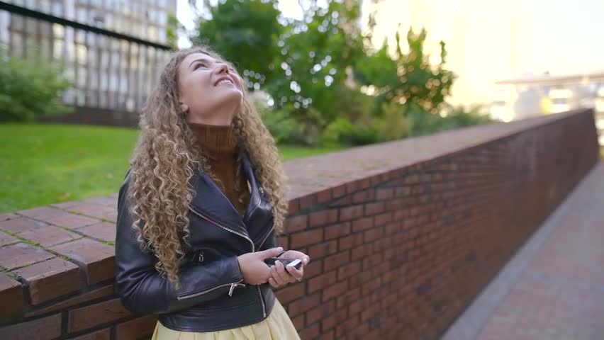 happy alone woman is laughing standing outdoors in street with mobile phone