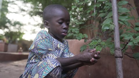 Littel African boy washing and cleaning his hands oudoors next to a tap in Bamako, Mali.