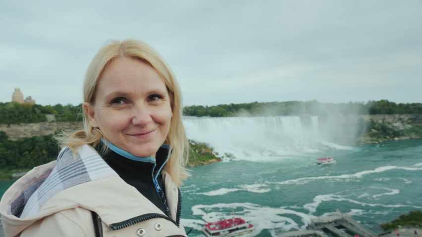 A young tourist stands against the backdrop of the Niagara Falls, smiling at the camera