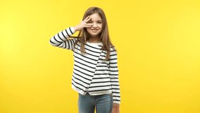 Funny child girl against an orange background embarrassed but laughing, is afraid to face something but is positive