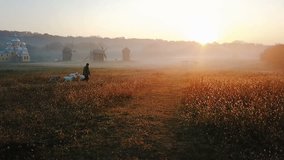 a shepherd leads a herd of goats to pasture. Early morning, golden sunlight. In the background is a field and mills. Morning in the Ukrainian village. Golden sunlight. Video footage