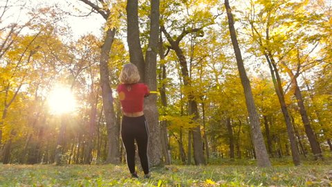 Young fit woman training with total resistance exercise system outdoors in the autumn forest. View from back. 
