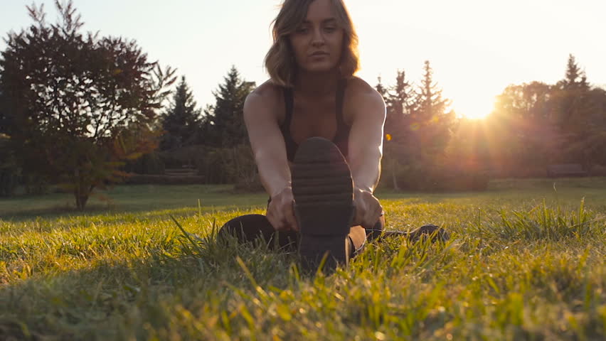 Young sporty woman sitting on the grass and doing stretching exercieses.