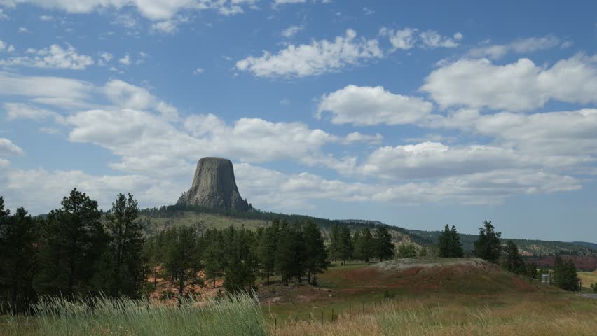 Extra wide steady shot of the Devil’s Tower in Wyoming, with tall grasses swaying in the breeze in the foreground
