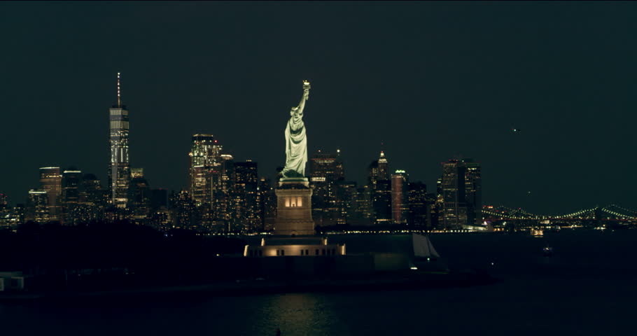 Aerial pan of the Statue of Liberty and Manhattan skyline, New York City, dark summer night light. Wide shot. 4k shot with a RED camera.
