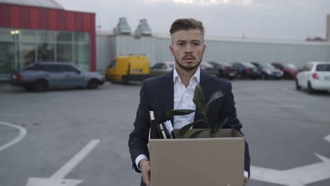 Emotional disappointed Corporate worker gets fired and walking down parking lot at the Roof with carton box and documents with a table flower. Lost His Job beacause a mistake.