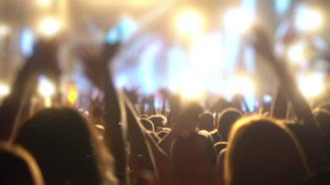 Happy people are watching an amazing musical concert. Merry fans jump and raise their hands up.
Crowd of excited fans applauding to popular band performing favorite song. A group of fans with phones