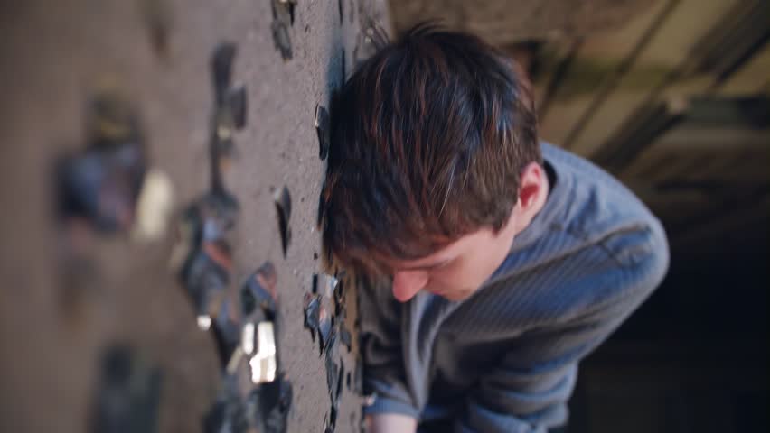 Nice looking caucasian guy with dark hair dressed in grey sweater with tattoo on arms lies on ground full of black glass shards then wakes up and looks around with puzzled feeling somewhere in street.