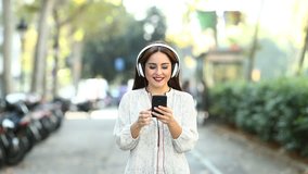 Front view of a happy woman walking towards camera listening to music with a smart phone recorded in slow motion
