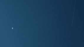 Travel concept - An airplane jet with contrail flying in sky with moon in daylight in background - Powered by Shutterstock - Get 15% off with code: PIKWIZARD15