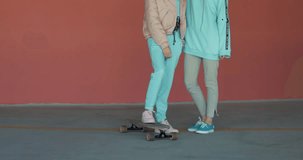 Two young woman standing with a longboard against red wall of car parking. Enjoying life. Urban city lifestyle. 4K video shooting by handheld gimbal