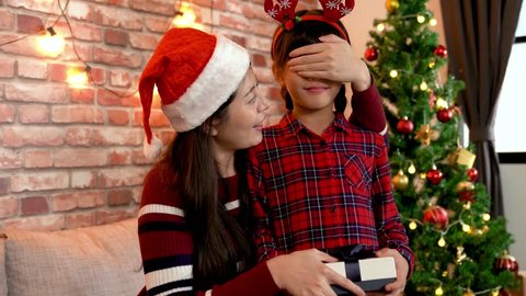 family and people on happy holidays in christmas celebration. happy mother with santa hat and little girl with gift box christmas tree background. mom closing kid's eyes while sending present.