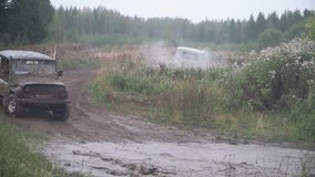 SUV at competition rides puddle of spray on dirt road. Clip. Cars take part in annual off-road races in countryside with fans in background in cloudy weather