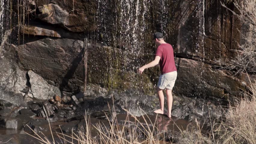 Man in a red t shirt standing underneath a waterfall in slow motion
