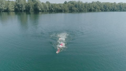 Aerial shot of athlete male training for iron man triathlon. Drone shot of man swimming in lake training for triathlon race.  Healthy lifestyle. Wellness, sport and fitness concept. Slow motion 
