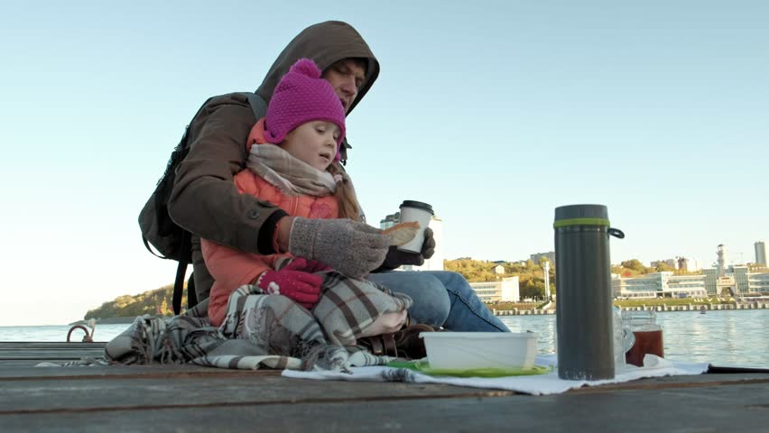 man and girl, father and daughter, sit in the river port, drink tea, picnic, laugh, in warm clothes 4k