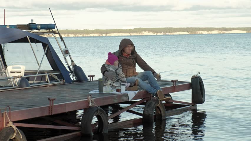 man and girl, father and daughter, sit in the river port, drink tea, picnic, laugh, in warm clothes 4k