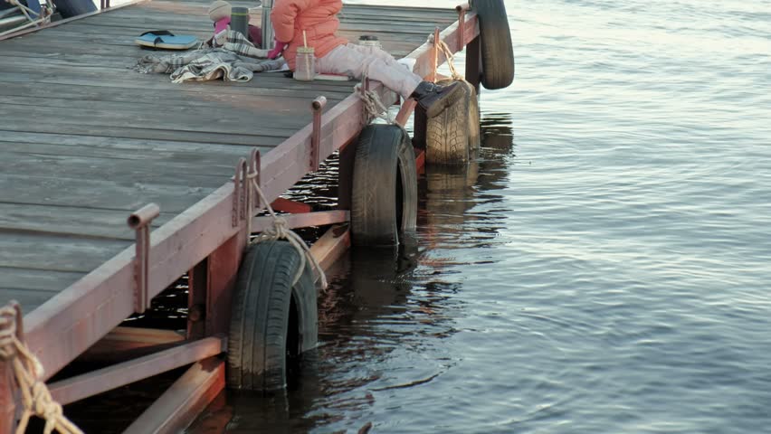 little girl, in warm clothes, sits on the bank of the river, on the river port, drinks hot tea, picnic 4k