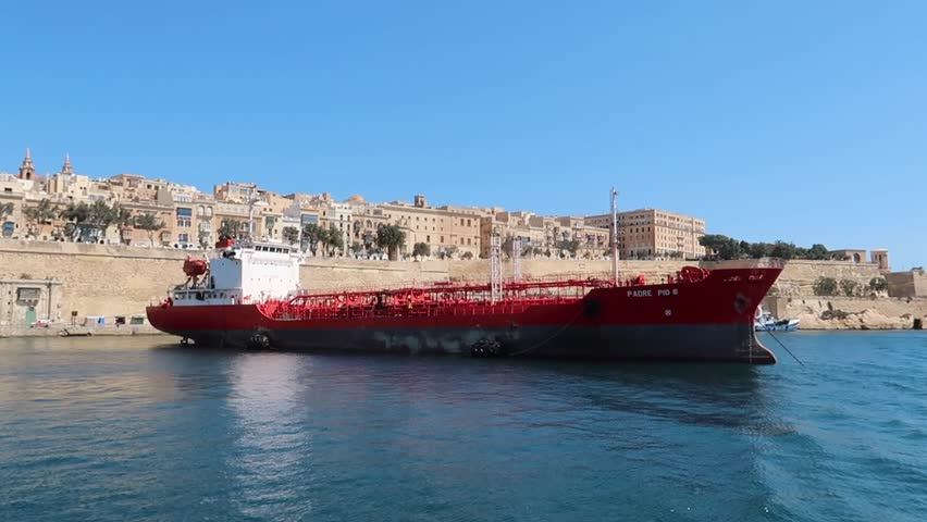 view from a moving boat of a red cargo ship at the coast of La Valetta in Malta