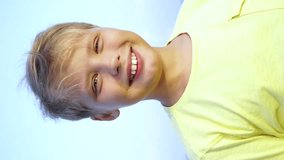 Closeup portrait of one happy handsome little caucasian kid isolated on blue sky background on summer beach during sunset time. Vertical orientation video of boy putting thumb up as sign of success.
