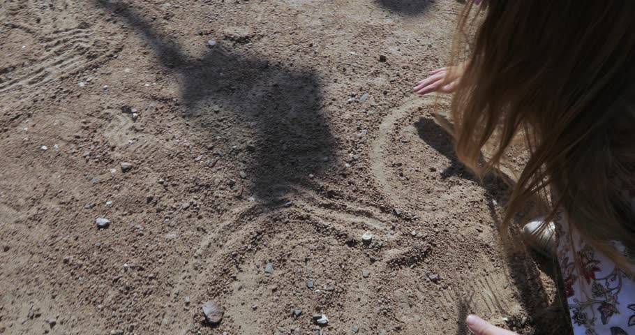 In the city park a child girl draws on the sand